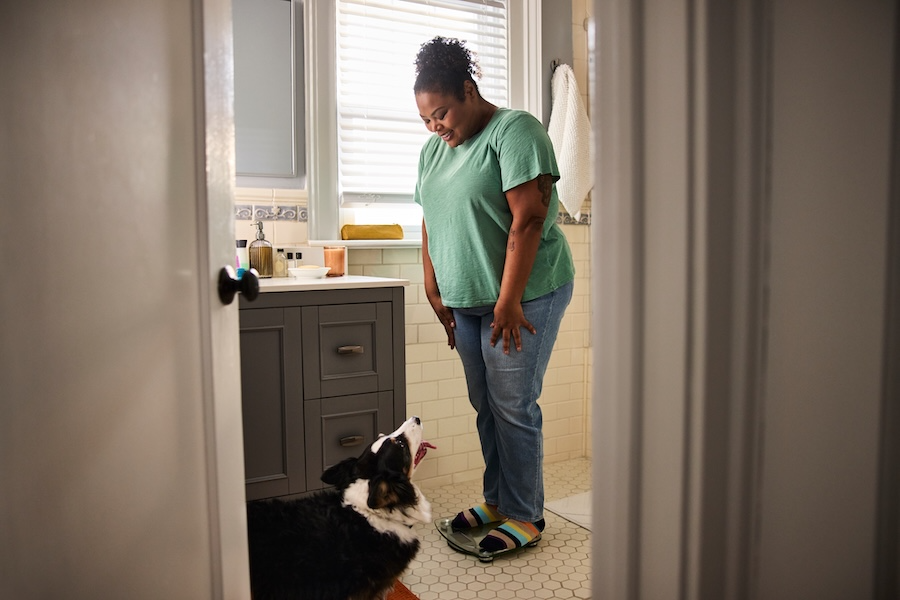 Person standing on a scale and smiling at their dog