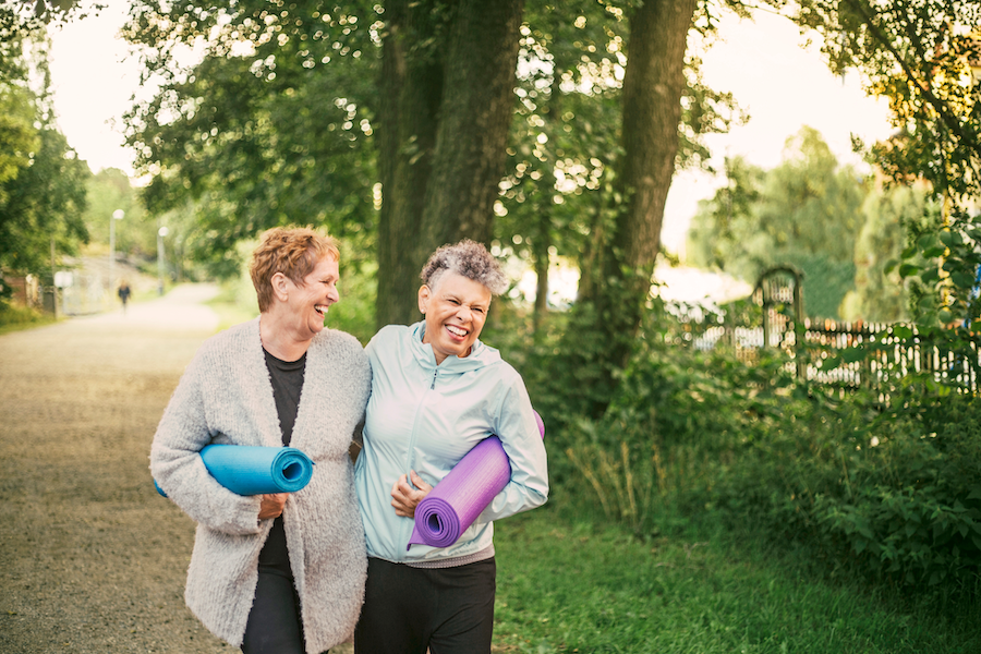 Two women walking in a park carrying yoga mats